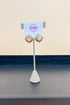 Pair of earrings on a stand with a branded card against a beige background