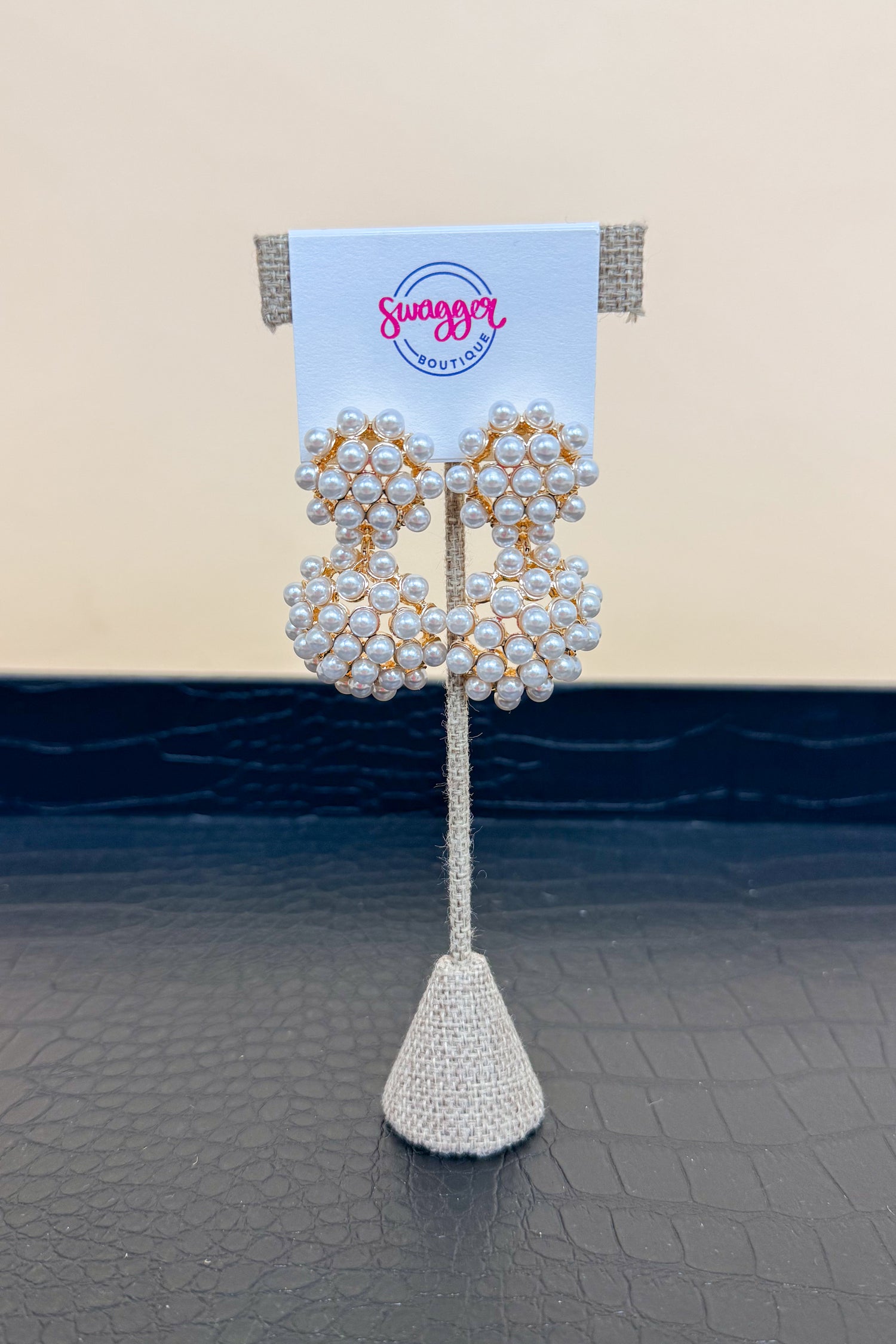 Pearl earrings on a decorative stand with a branded card against a neutral background