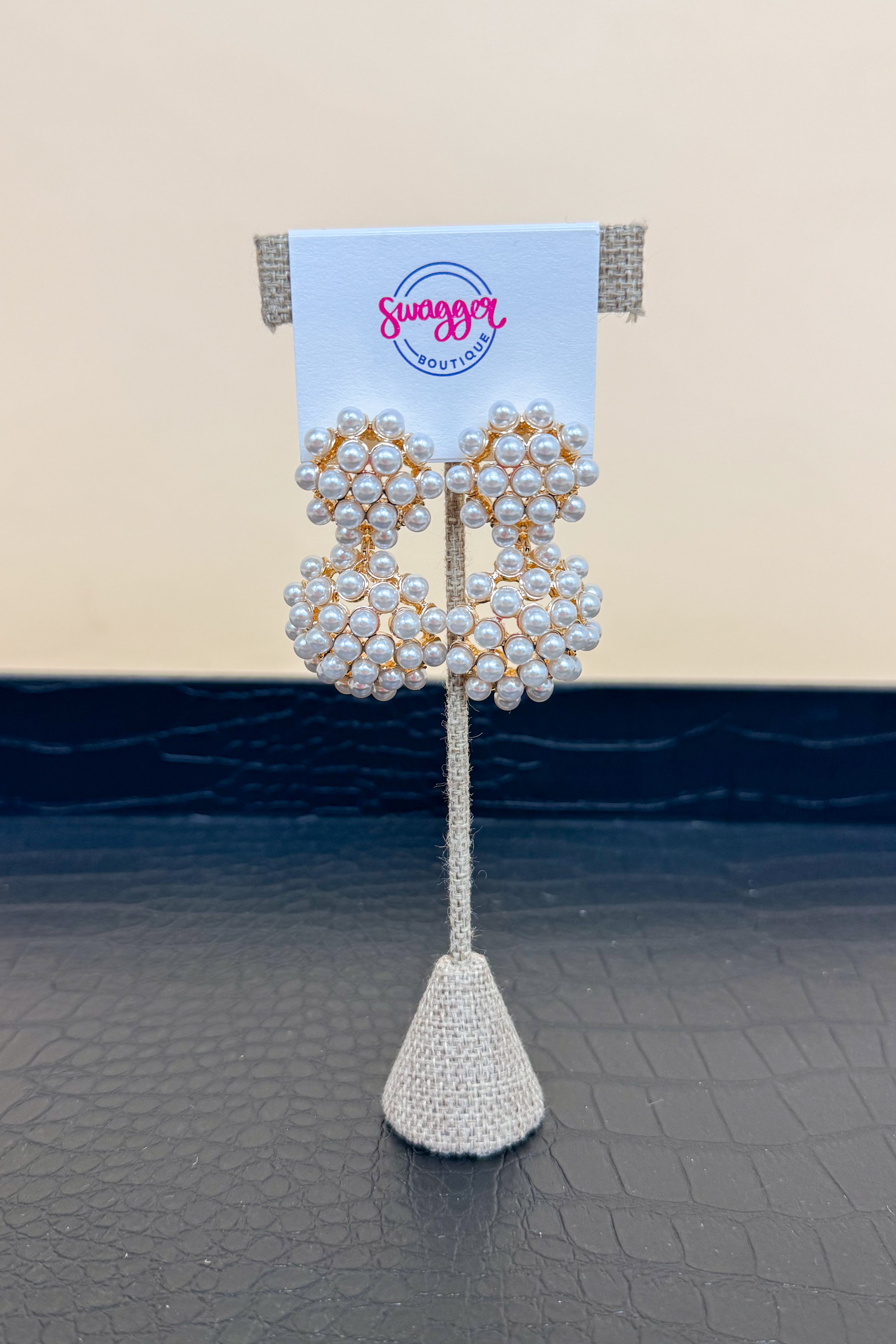 Pearl earrings on a decorative stand with a branded card against a neutral background
