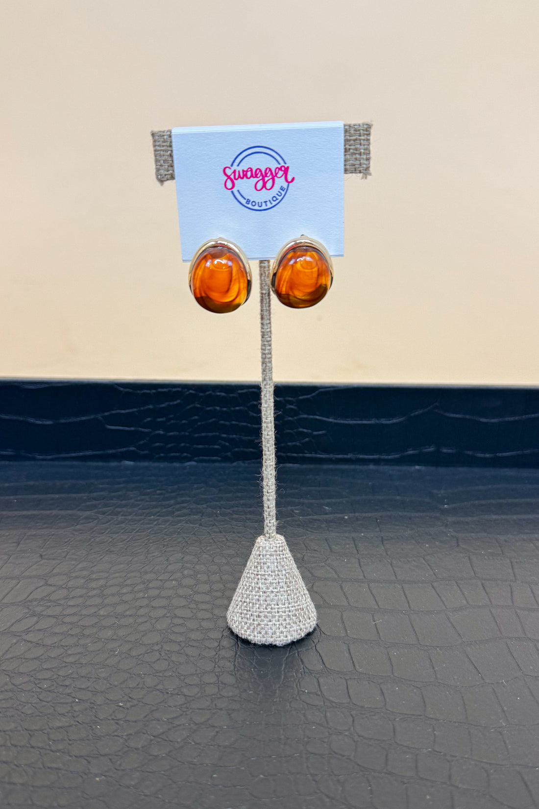 Pair of amber earrings on a stand with a branded card against a beige and black background