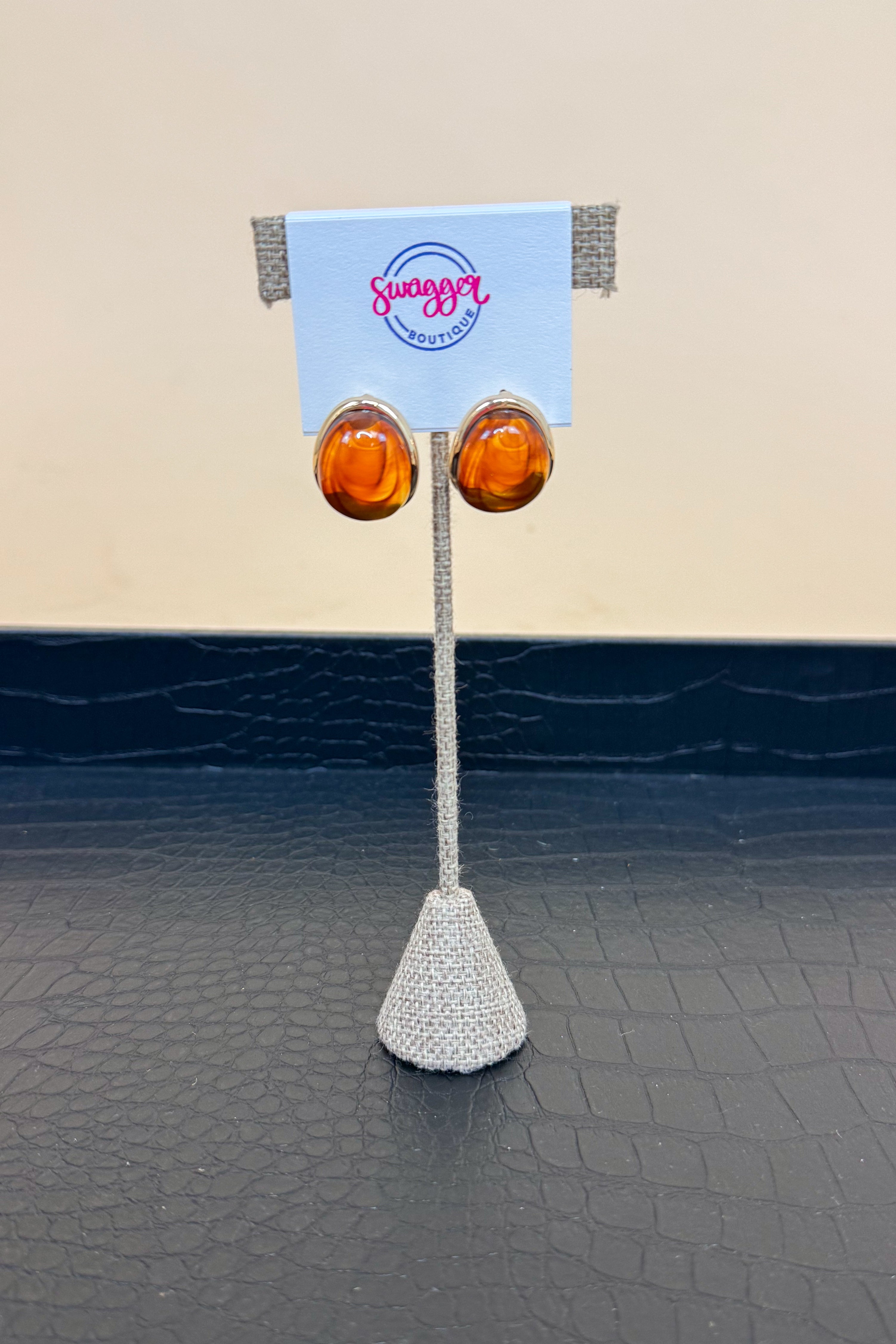 Pair of amber earrings on a stand with a branded card against a beige and black background