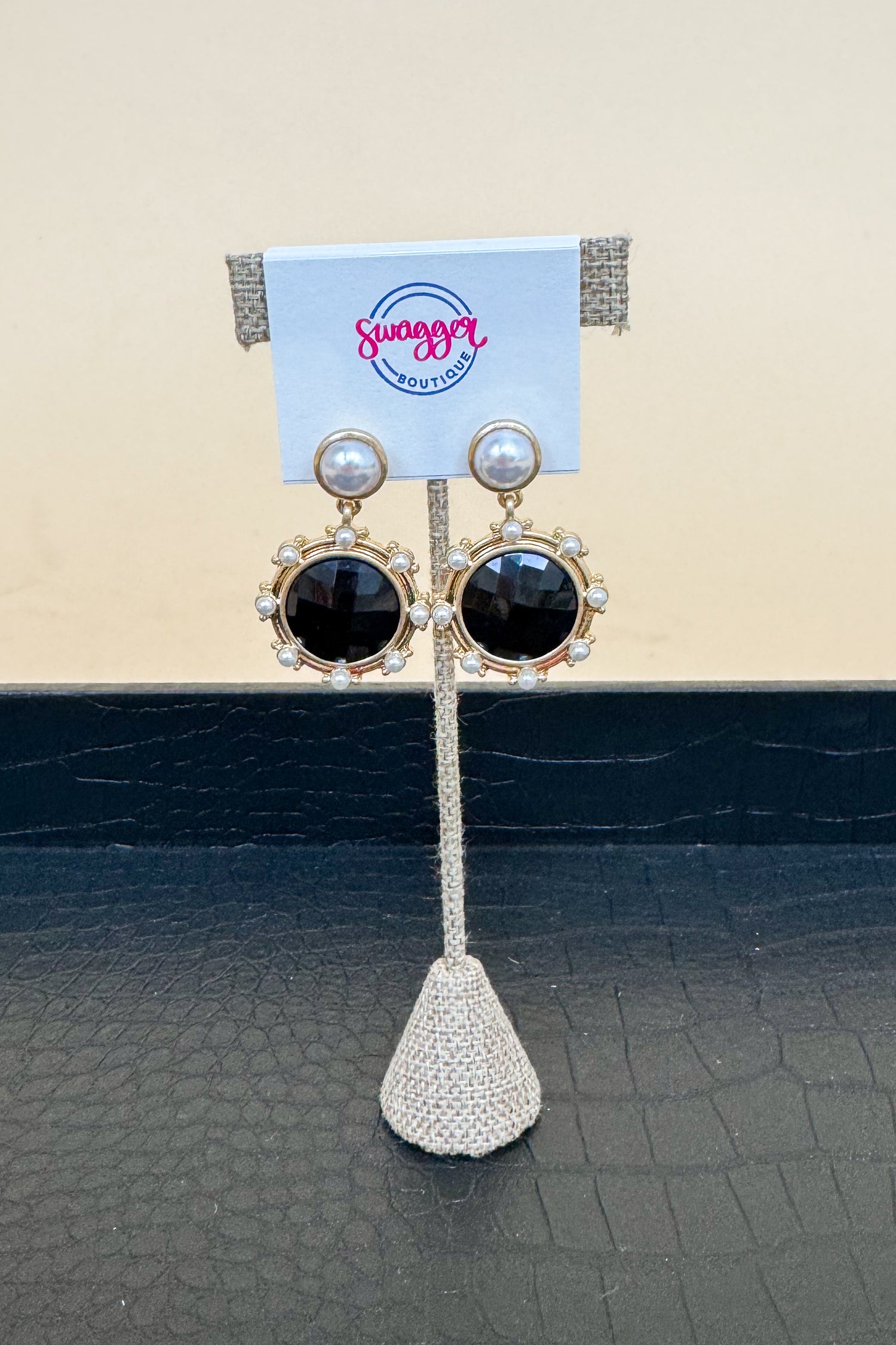 Pair of earrings on a display stand with a  brand card in the background.