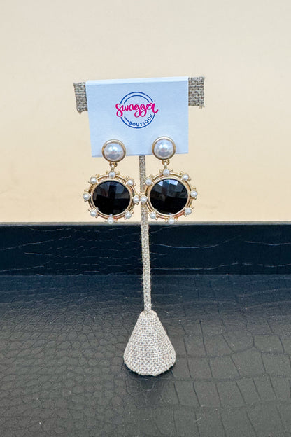 Pair of earrings on a display stand with a  brand card in the background.