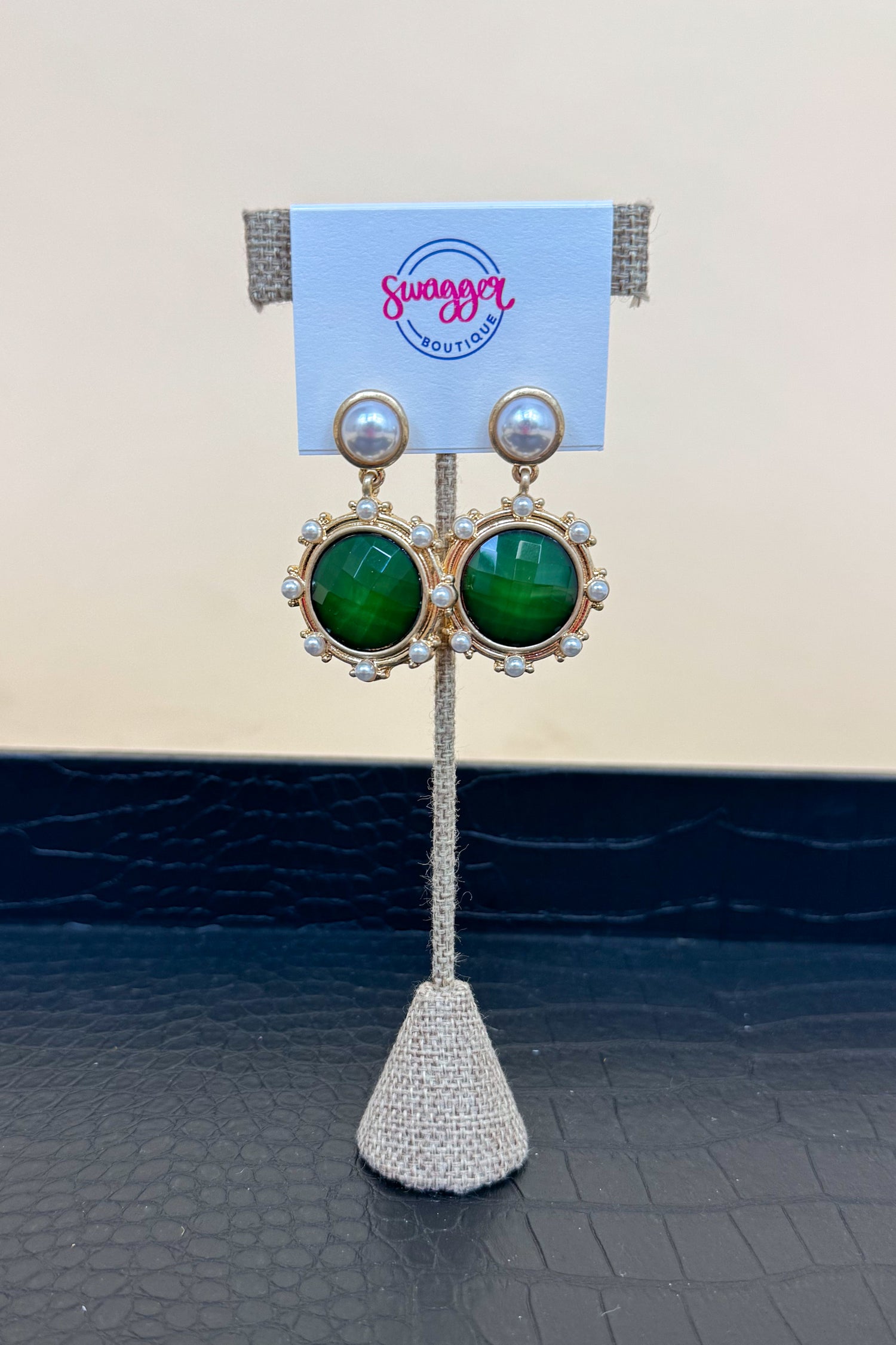 Gold earrings with green gemstones on a branded stand.