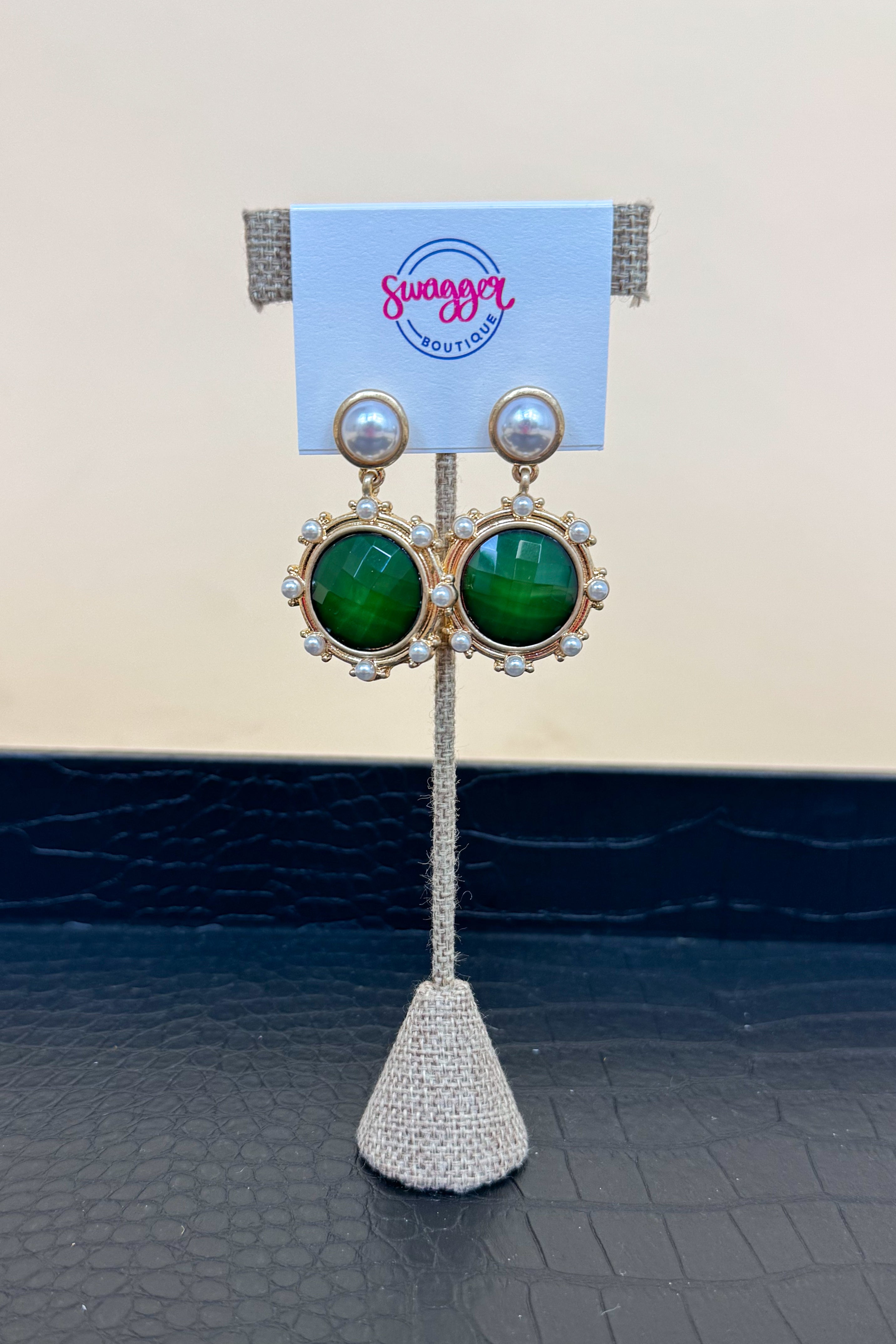 Gold earrings with green gemstones on a branded stand.