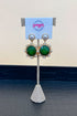 Gold earrings with green gemstones on a branded stand.
