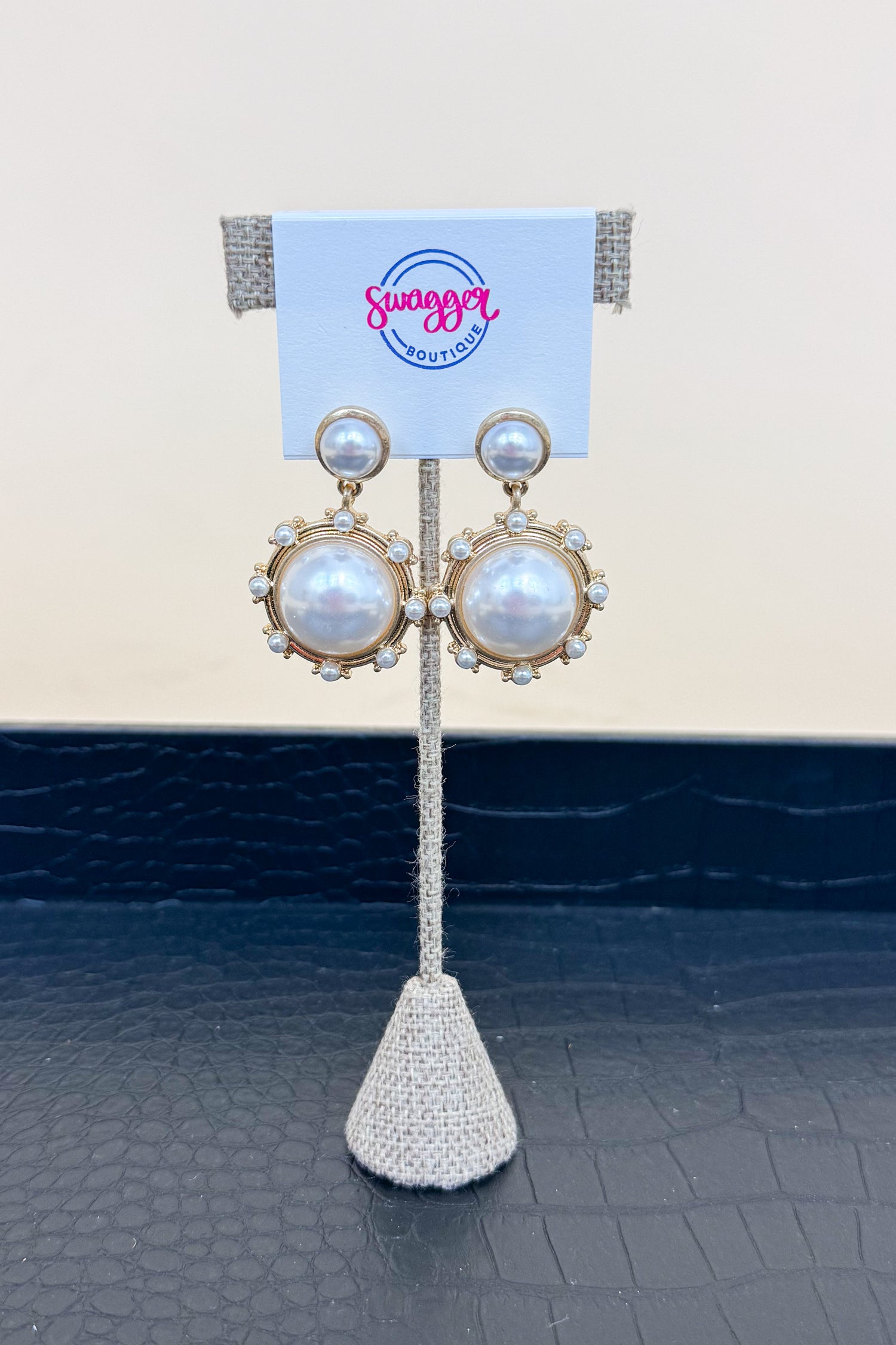 Pair of pearl earrings on a stand with a branded card in the background
