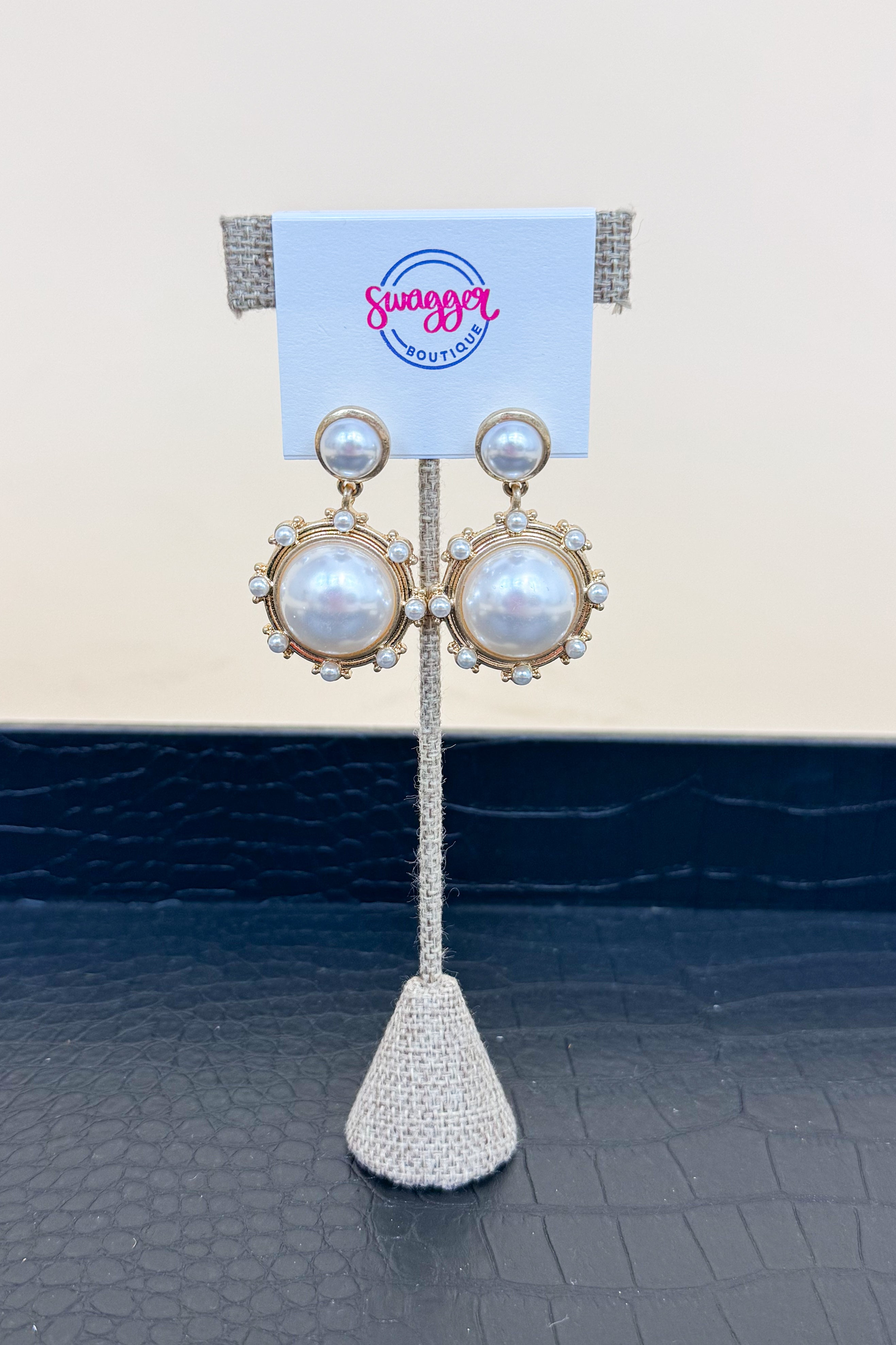 Pair of pearl earrings on a stand with a branded card in the background
