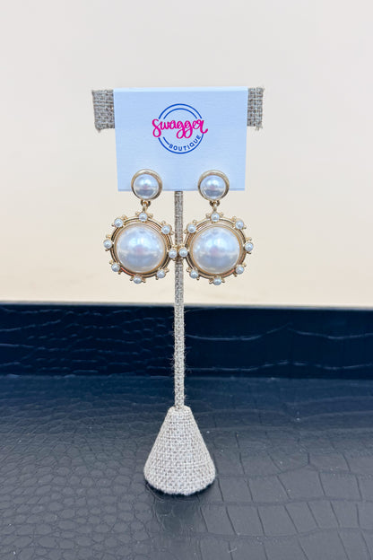 Pair of pearl earrings on a stand with a branded card in the background