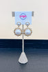 Pair of pearl earrings on a stand with a branded card in the background