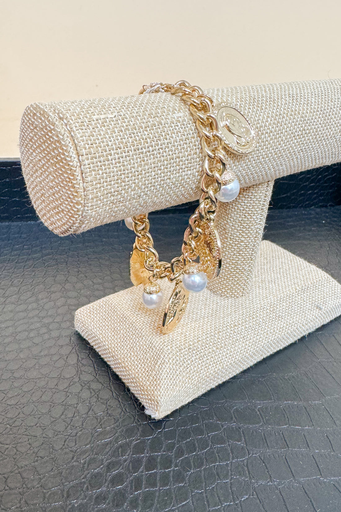 Gold bracelet with pearls on a beaded stand against a neutral background
