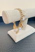 Gold bracelet with pearls on a beaded stand against a neutral background