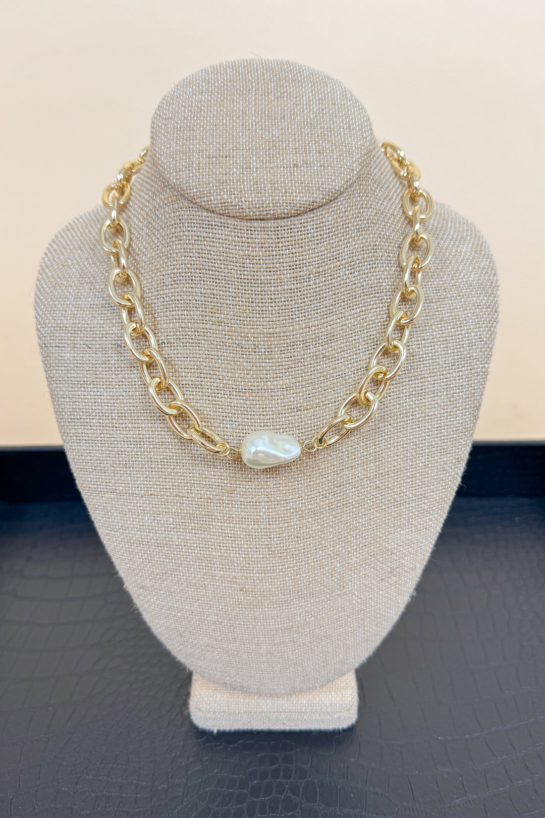 Gold chain necklace with a pearl pendant on a gray bust