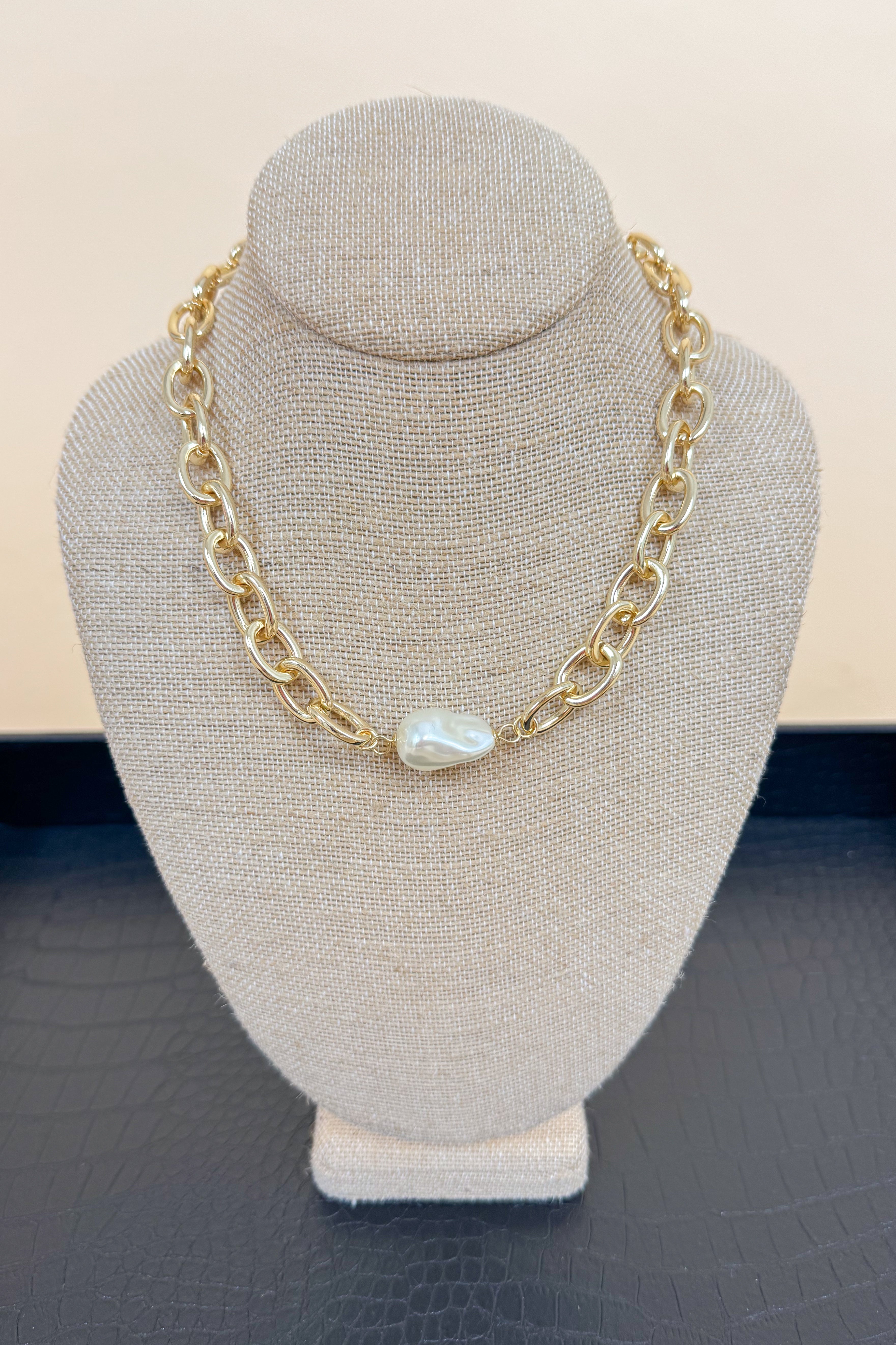 Gold chain necklace with a pearl pendant on a gray bust