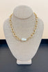 Gold chain necklace with a pearl pendant on a gray bust