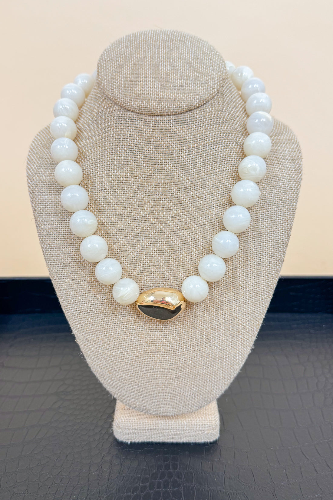 White necklace with a gold clasp on a beige mannequin bust against a beige background