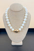 White necklace with a gold clasp on a beige mannequin bust against a beige background