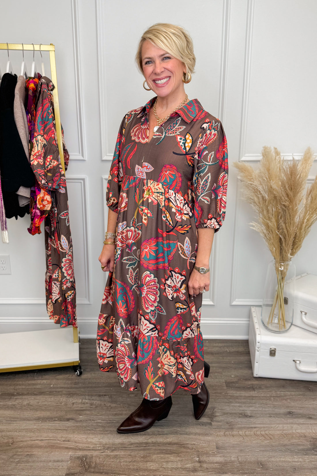 Woman wearing a floral dress standing in a room with a rack of clothes and decorative items.