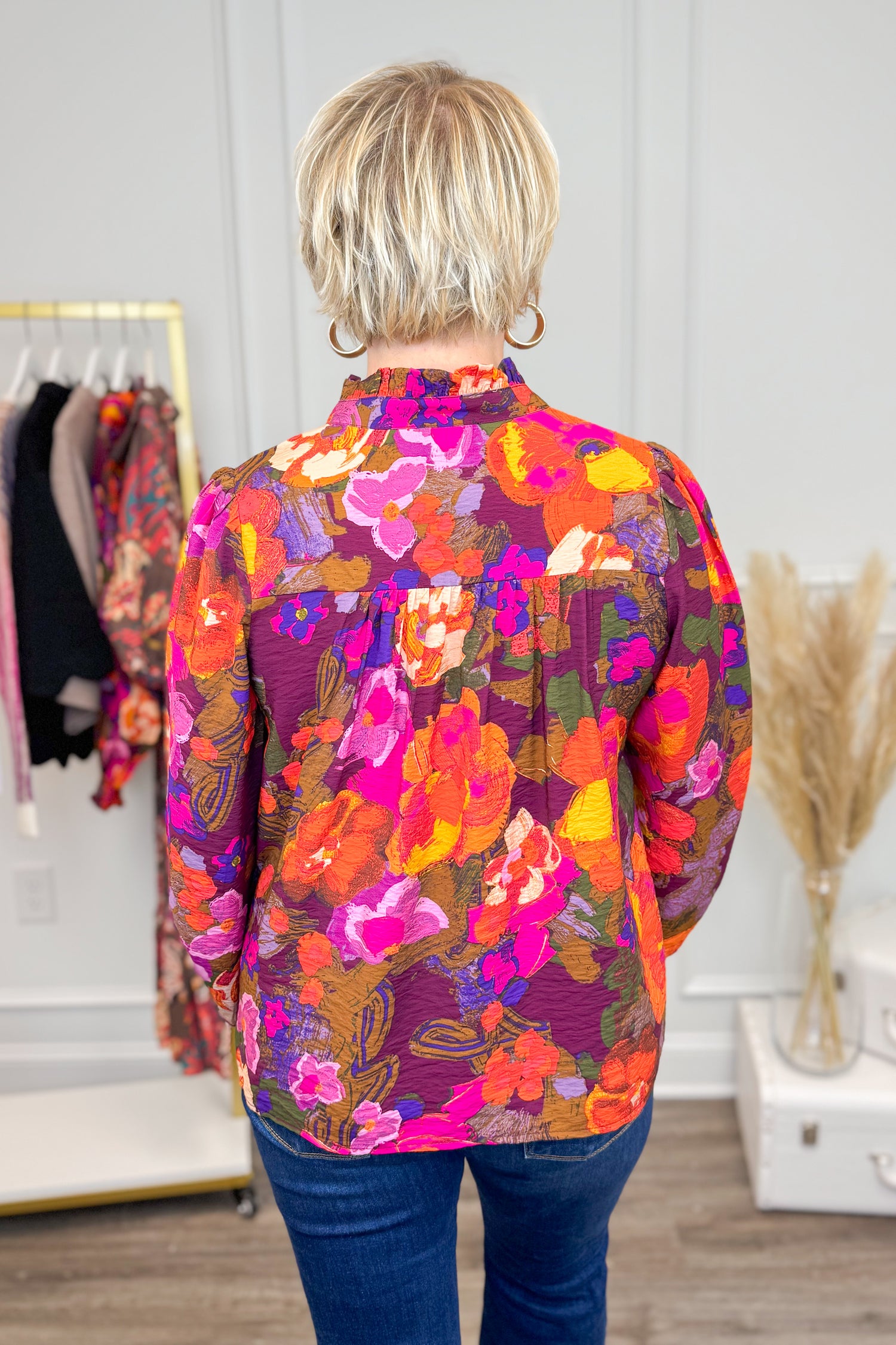 Person wearing a colorful floral shirt in a room with clothing racks and decor.