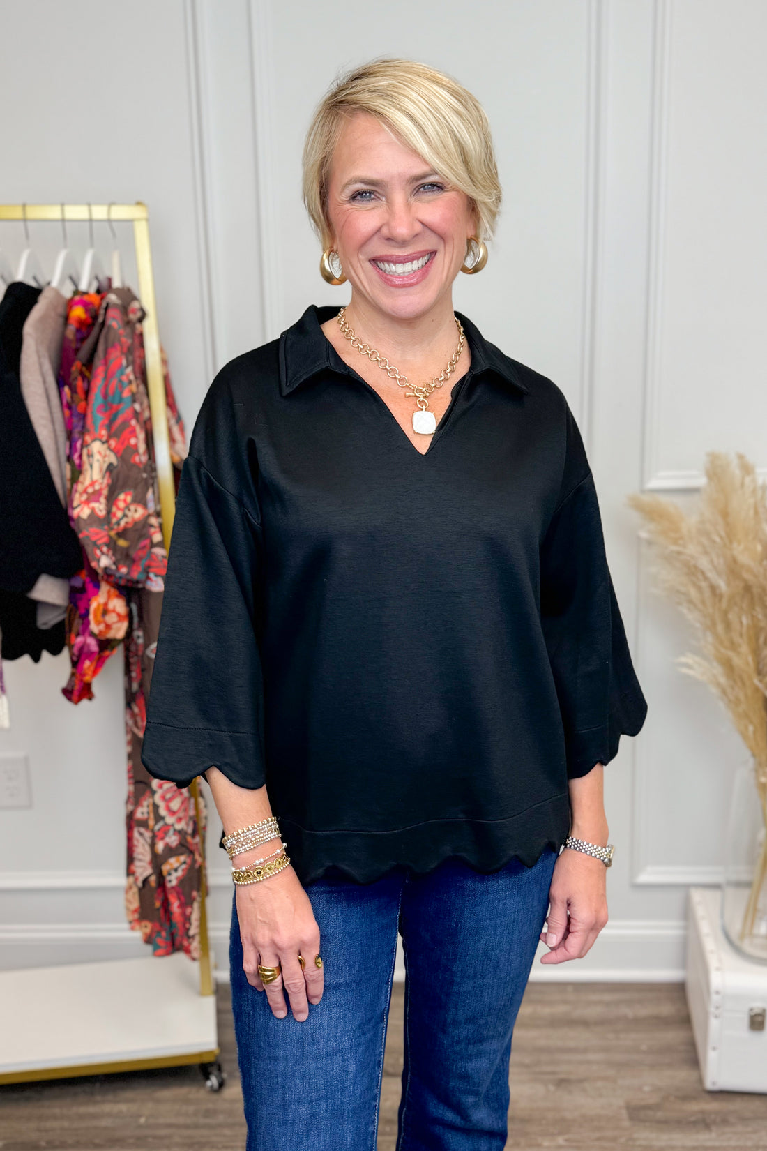 Woman wearing a black blouse and blue jeans in a room with clothing racks.