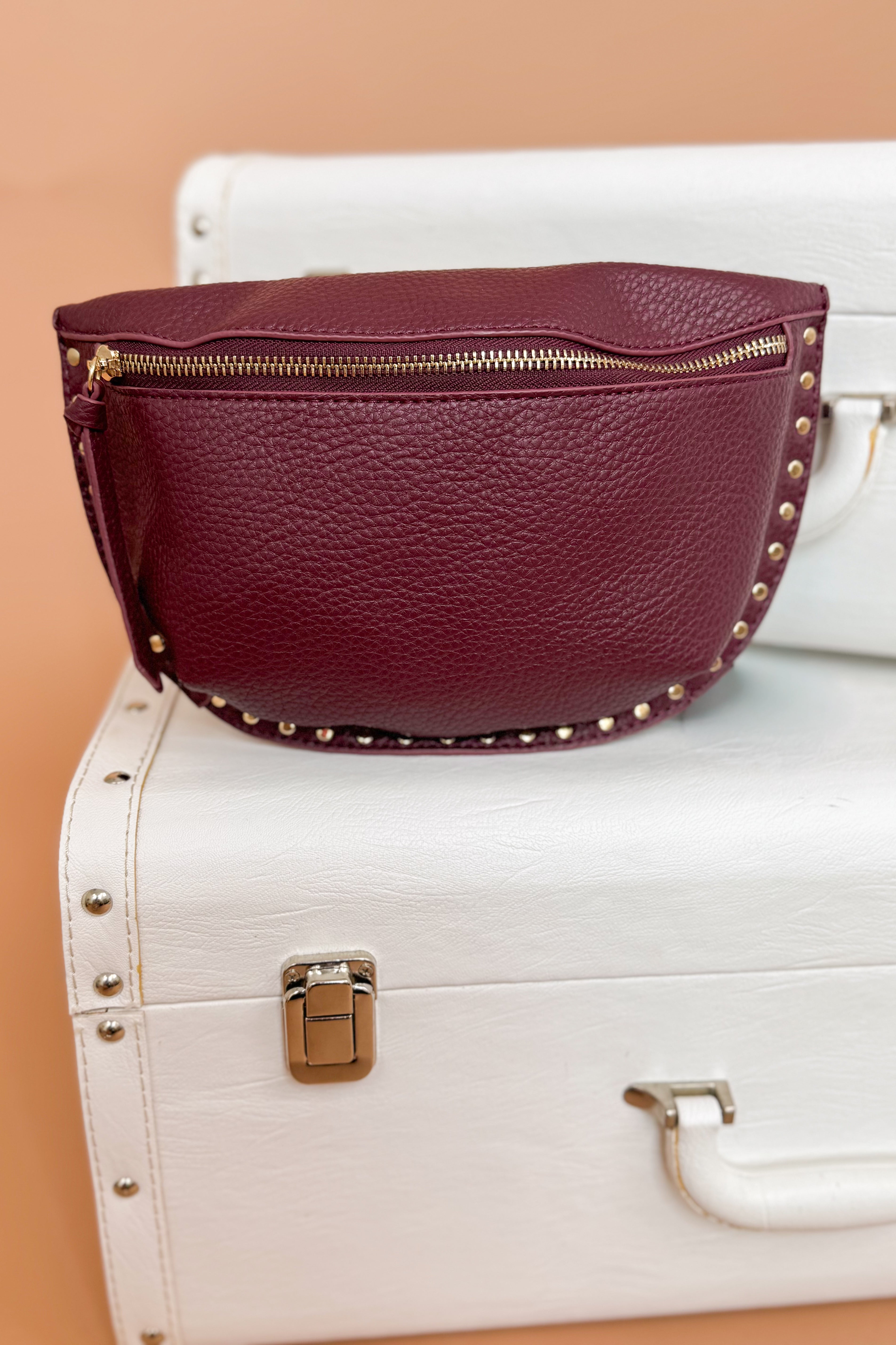 Maroon leather bag with gold studs on a white suitcase against a beige background