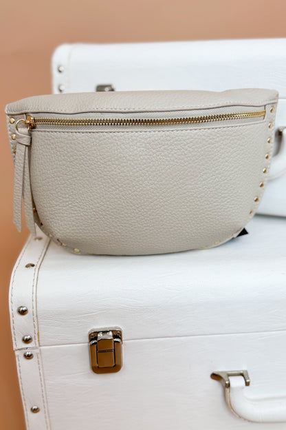 Beige leather bag with gold zipper on a white suitcase against a beige background