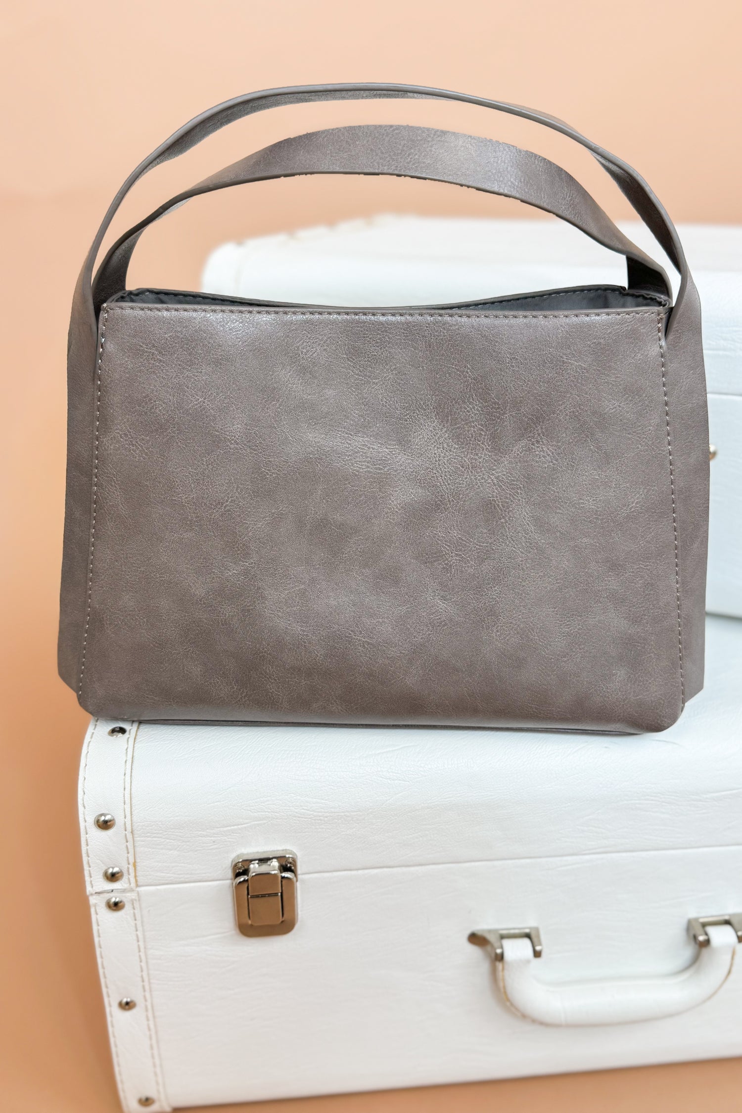 Gray handbag on a white suitcase with a beige background