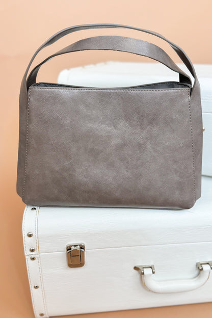 Gray handbag on a white suitcase with a beige background