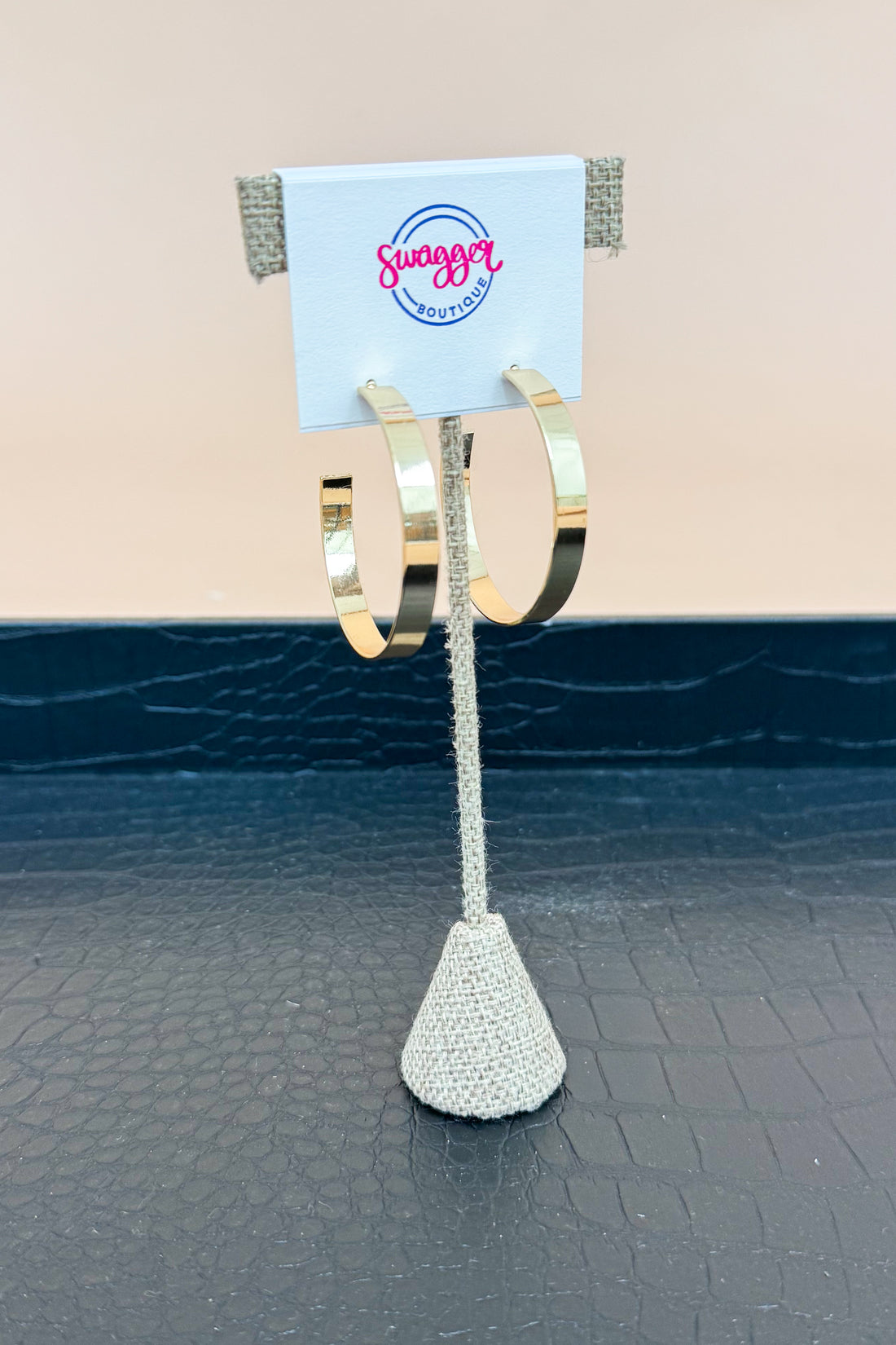 Gold hoop earrings on a stand with a branded card against a neutral background