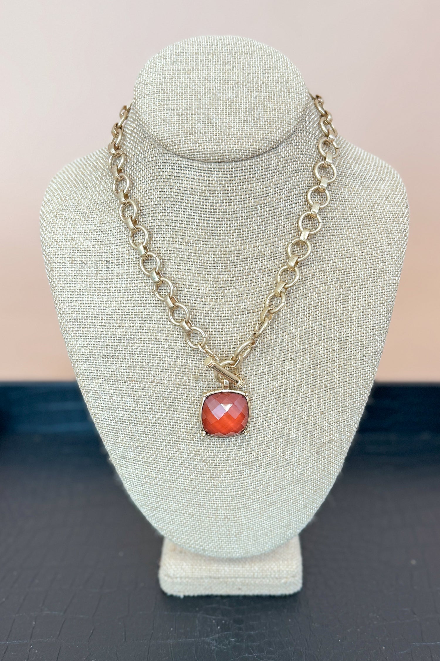Necklace with a brown pendant on a gray bust against a beige background