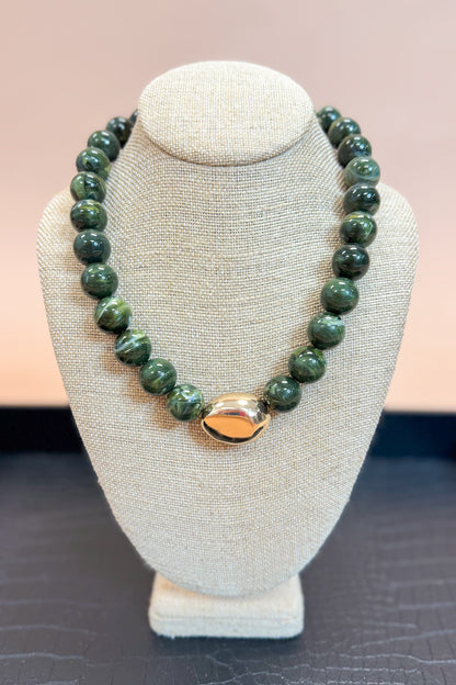 Green beaded necklace with a gold clasp on a gray bust