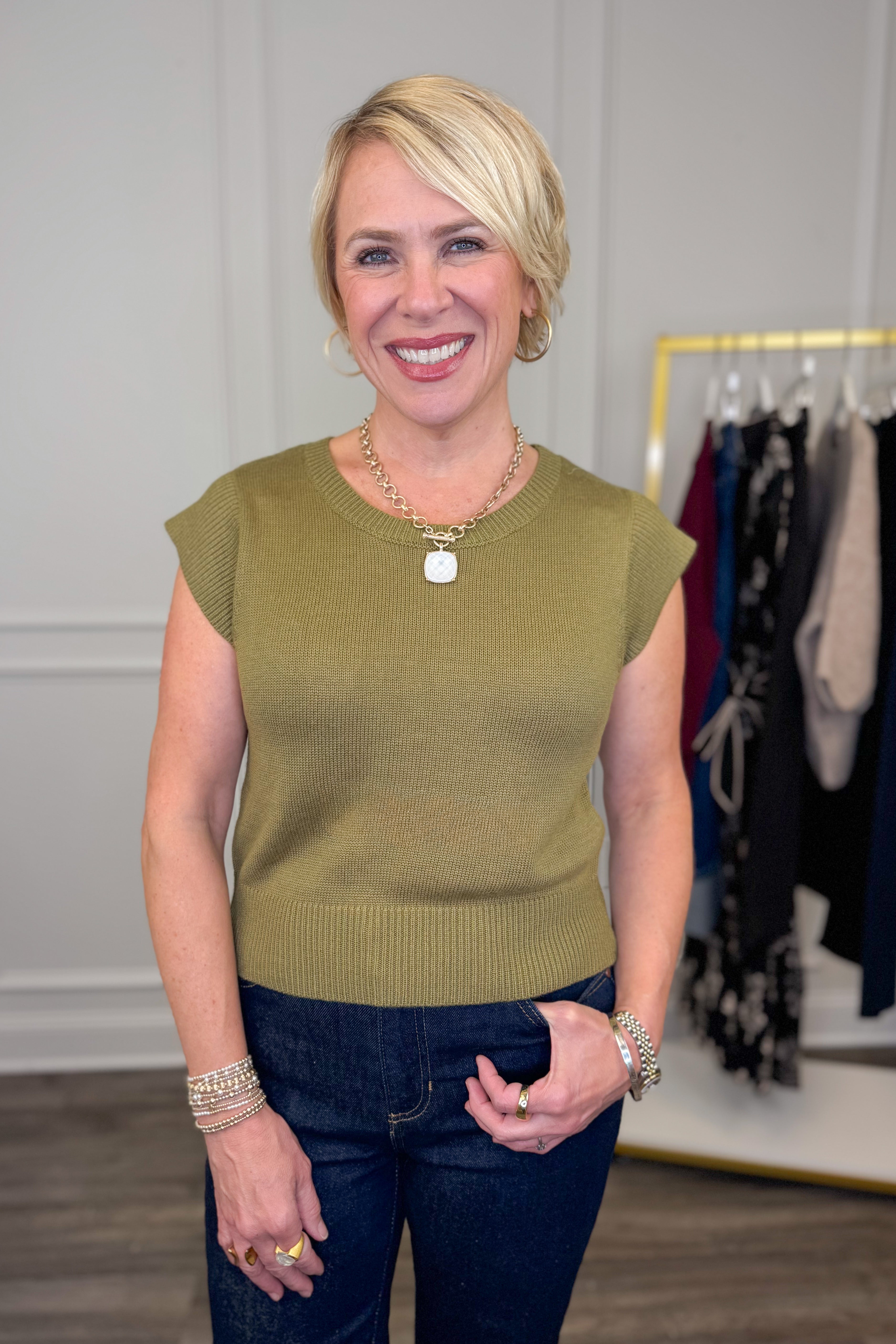 Woman wearing a green sleeveless top and blue jeans in a clothing store.