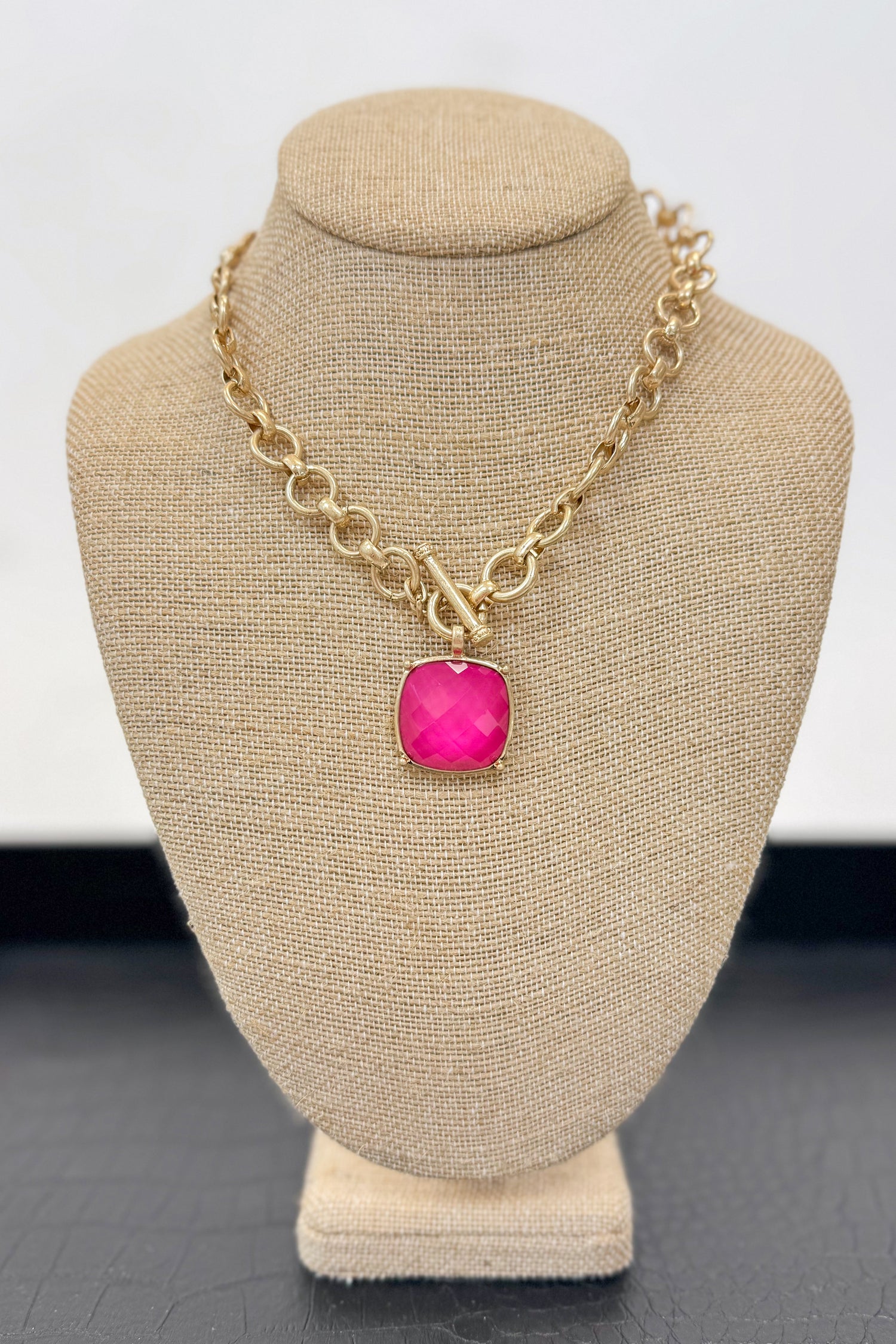 Gold necklace with a pink pendant on a beige bust against a white background