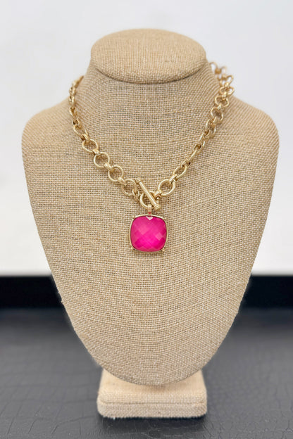 Gold necklace with a pink pendant on a beige bust against a white background