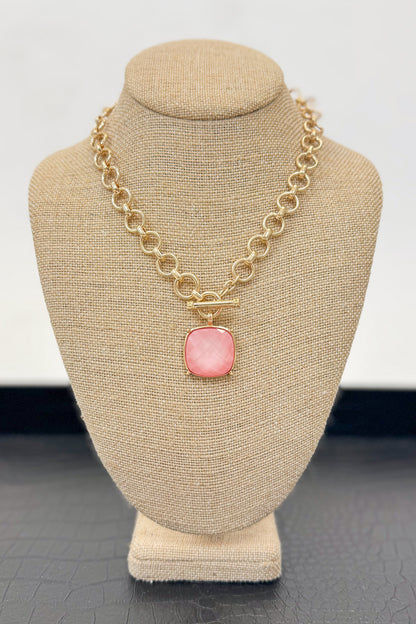 Gold necklace with a light pink pendant on a beige bust against a white background