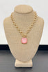 Gold necklace with a light pink pendant on a beige bust against a white background