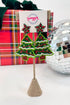 Decorative Christmas tree earrings on a stand with a gift box and disco ball in the background