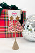 Decorative earrings shaped like Christmas trees on a stand with a gift box and disco ball in the background.