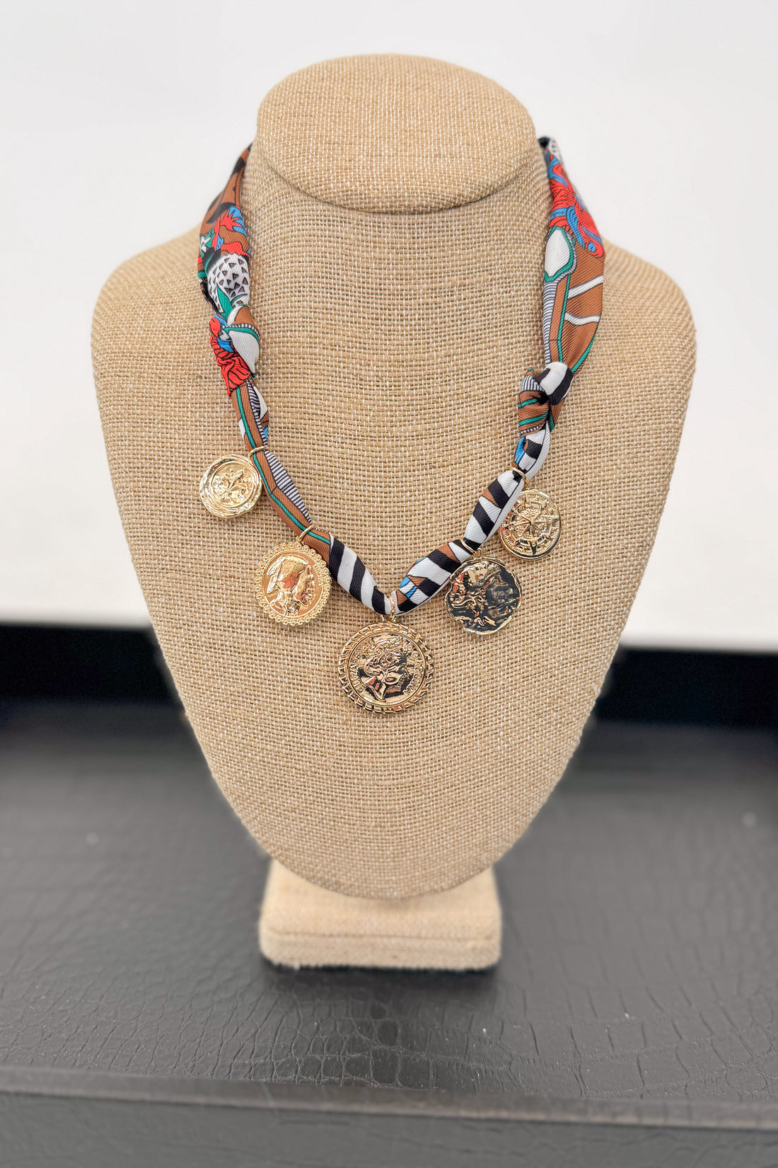 Necklace with colorful fabric strap and gold coins on a beige bust