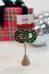 Christmas-themed earrings with wreath and red bows on a stand