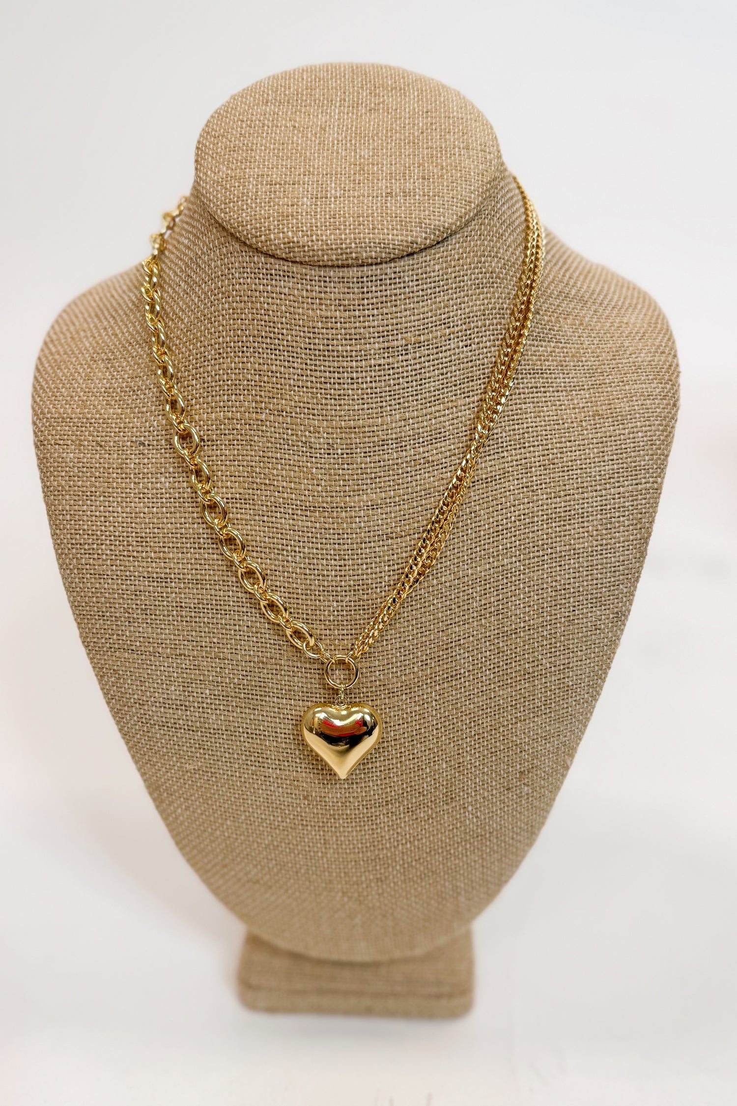 Gold chain necklace with a heart pendant on a beige bust