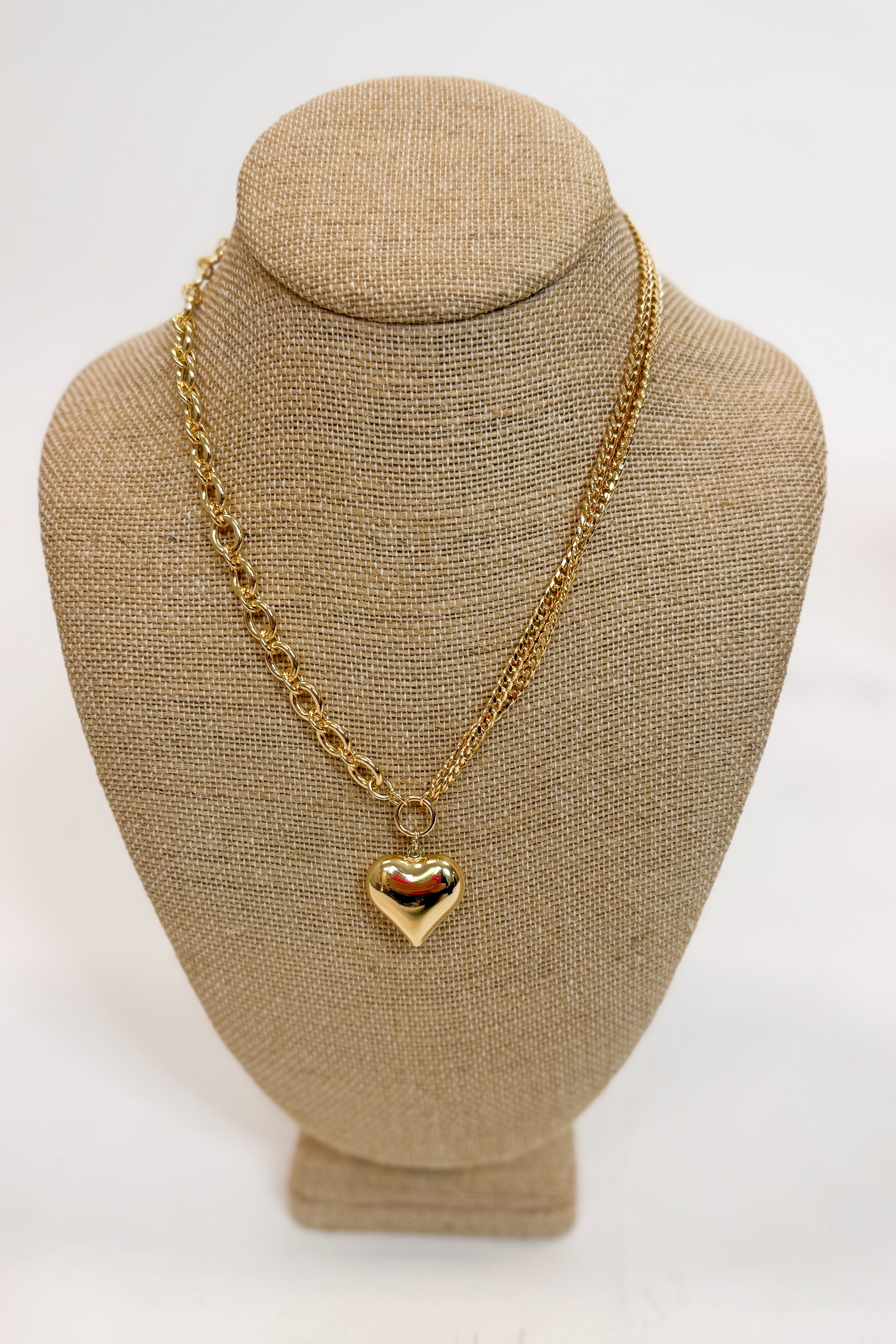 Gold chain necklace with a heart pendant on a beige bust