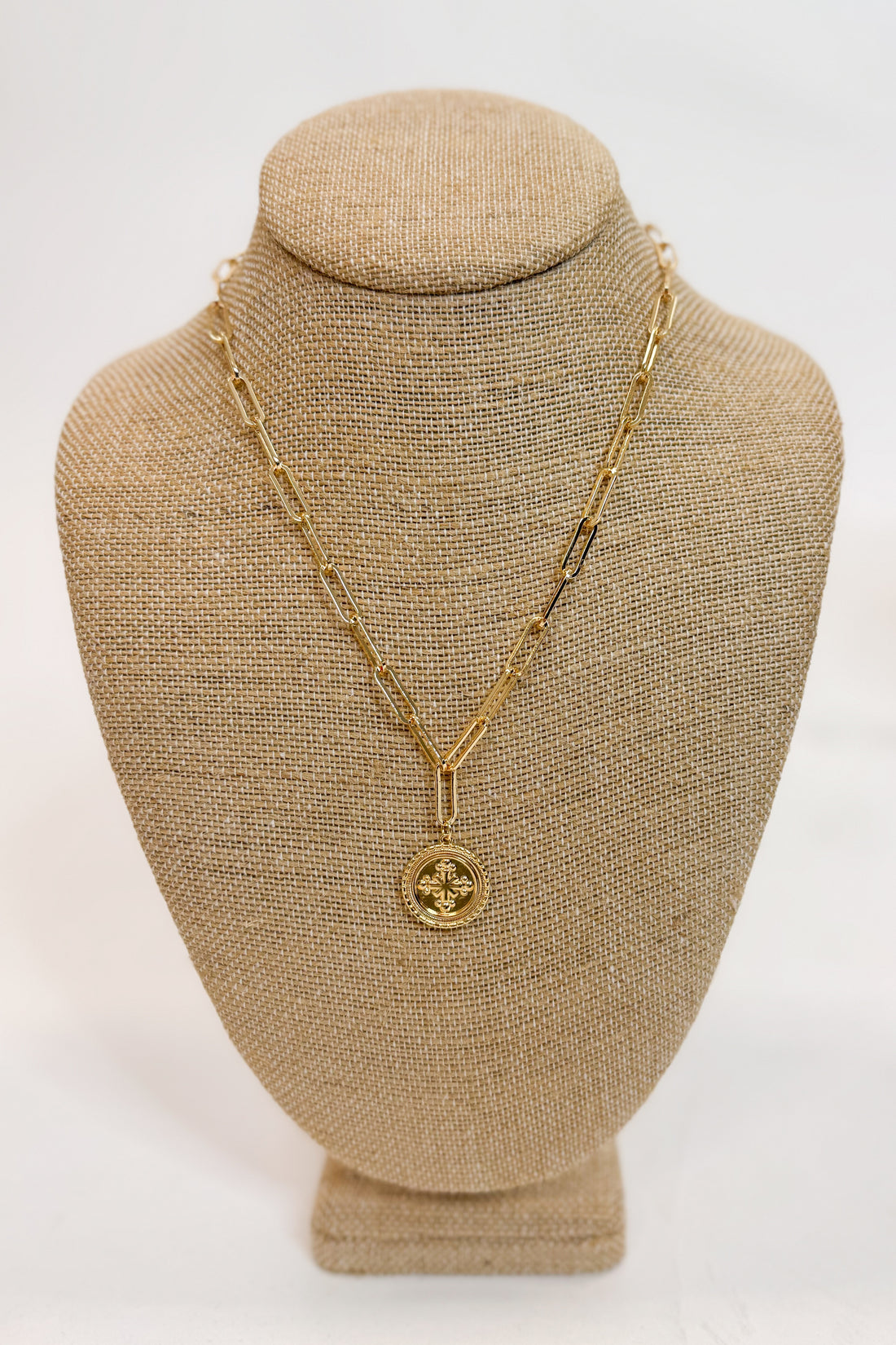 Gold necklace with a pendant on a beige bust against a white background