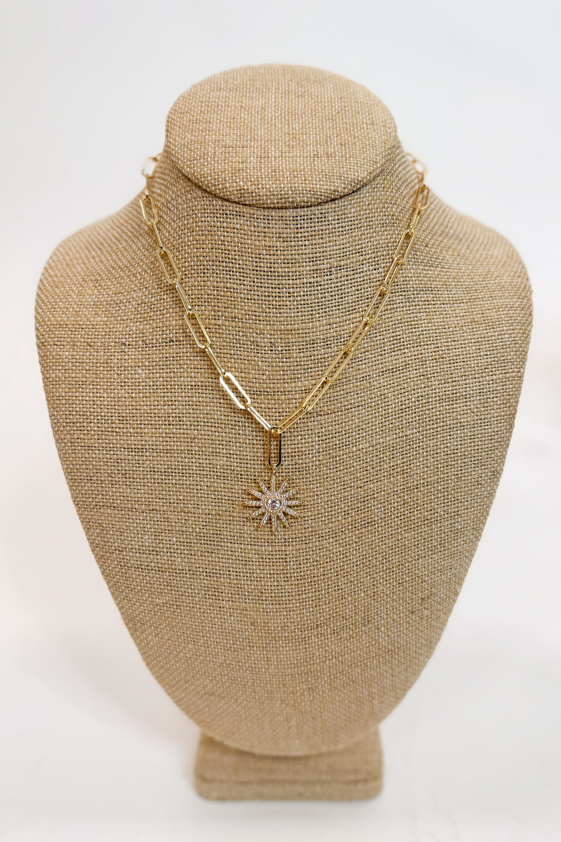 Gold necklace with a star-shaped pendant on a beige bust against a white background