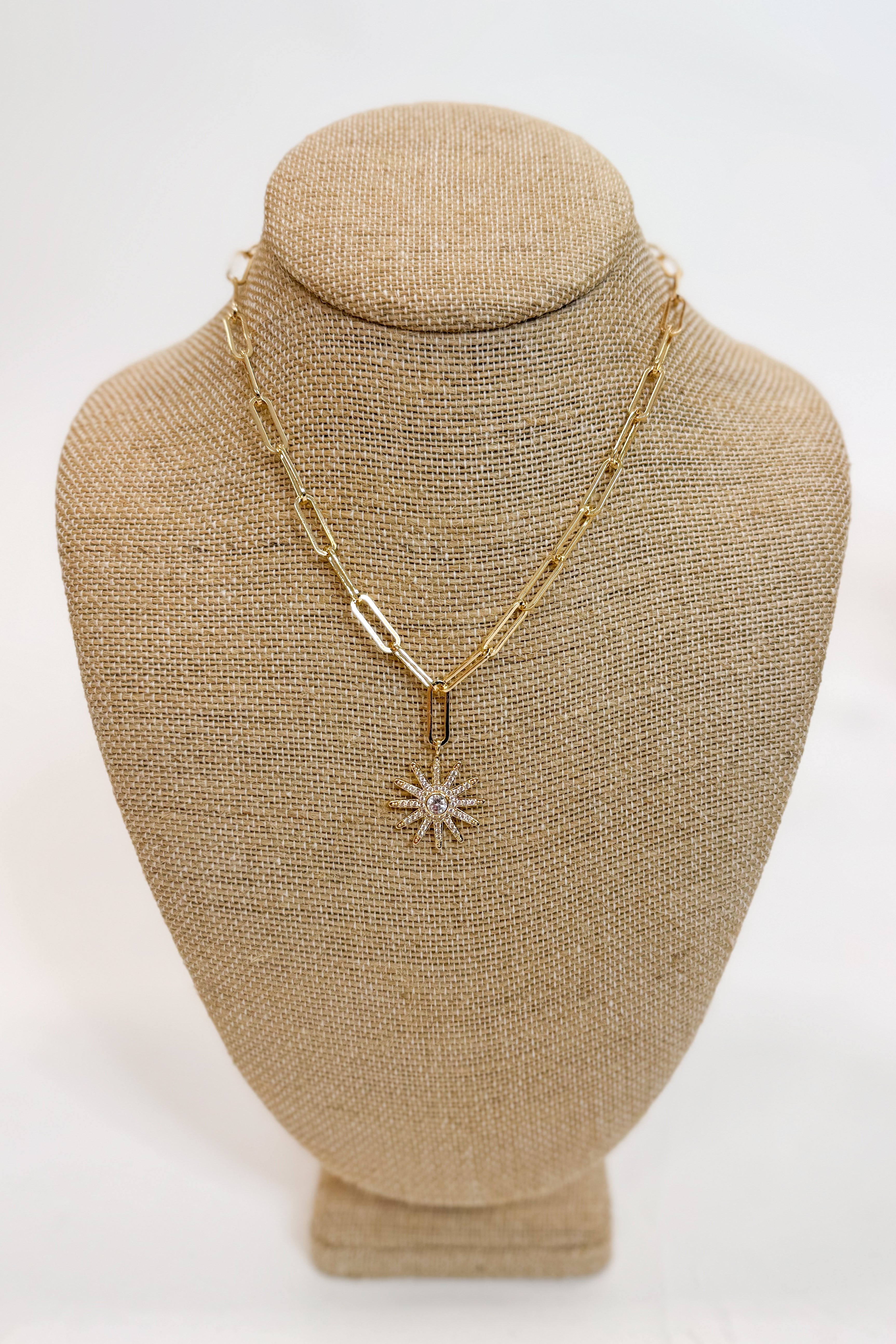 Gold necklace with a star-shaped pendant on a beige bust against a white background