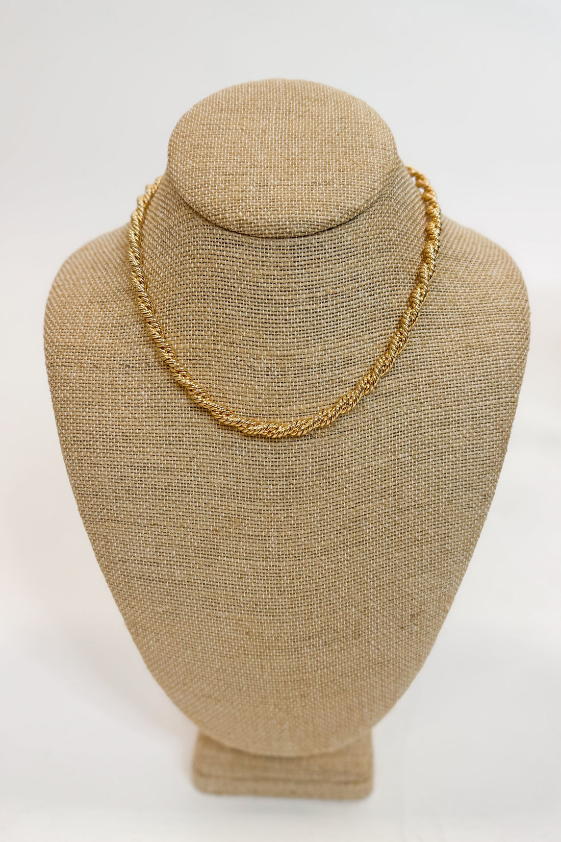 Gold chain necklace on a beige mannequin bust against a white background