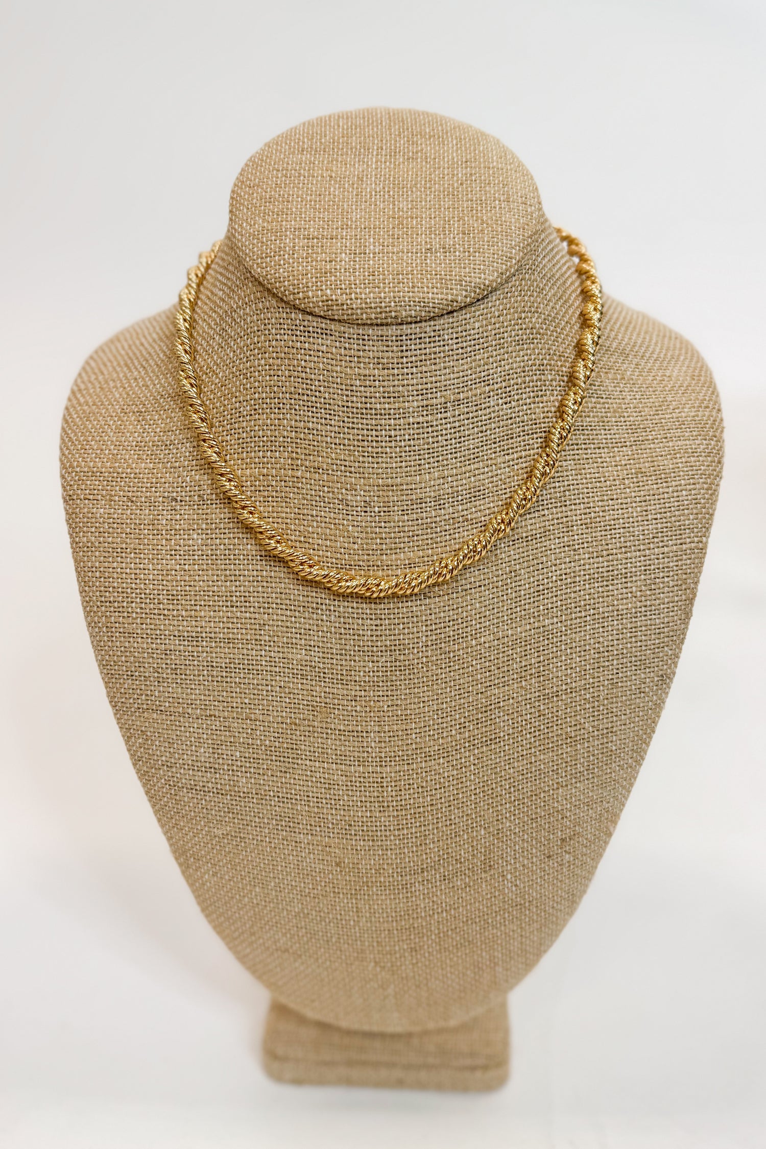 Gold chain necklace on a beige mannequin bust against a white background