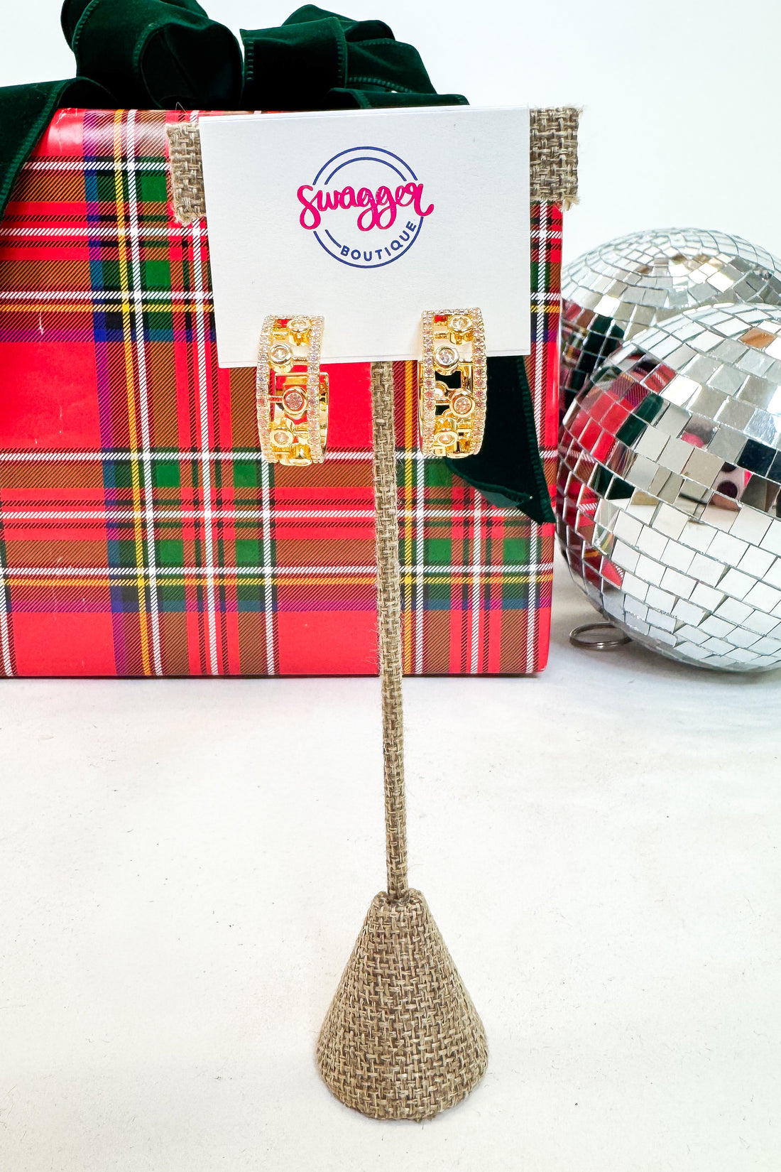 Decorative stand with earrings, plaid gift box, and disco ball on a white background