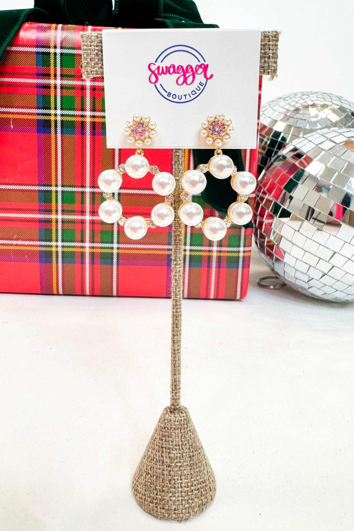 Decorative earrings with a plaid gift box and disco ball in the background