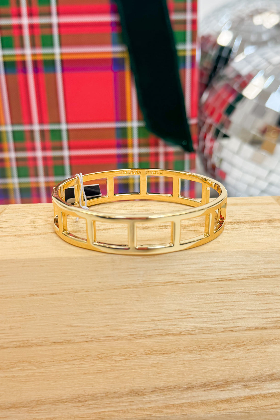 Gold bracelet on a wooden surface with a plaid fabric background